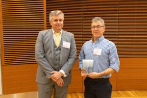 two men stand, one is holding a glass award