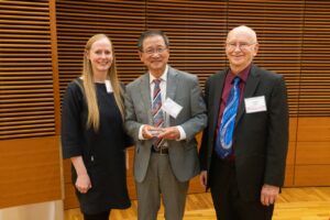 three people stand, one is holding a glass plaque