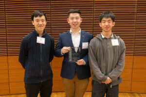 three male students pose, one with a plaque