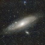 a mostly black image with a wispy galaxy at the center and small white dots (stars) surrounding it