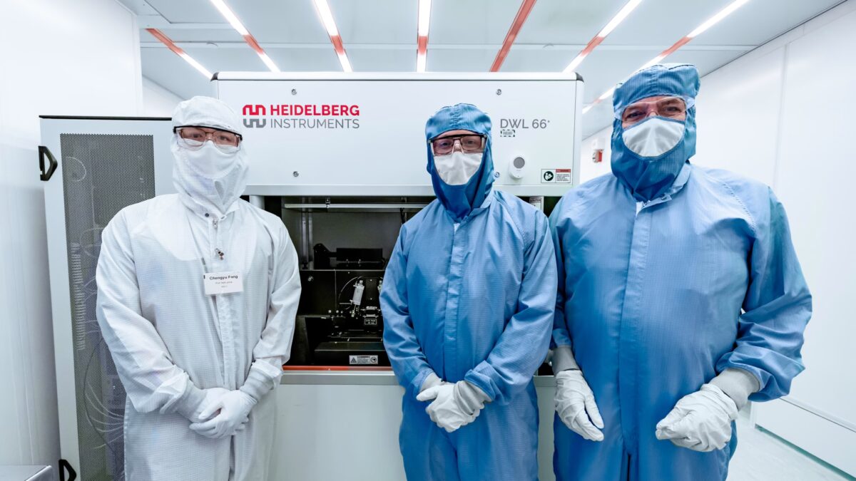 three people dressed head-to-toe in anti-static suits stand in an all-white clean room