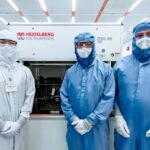 three people dressed head-to-toe in anti-static suits stand in an all-white clean room
