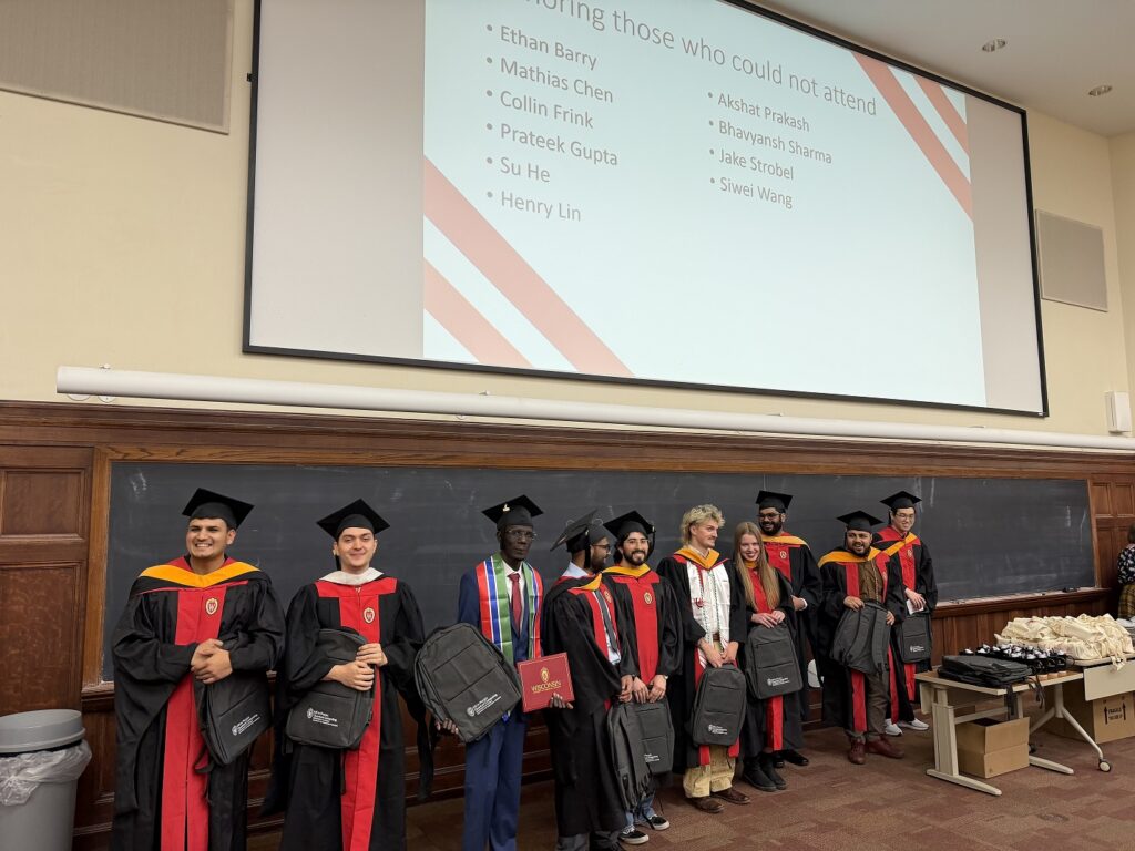 students wearing graduation robes stand in the front of a lecture hall
